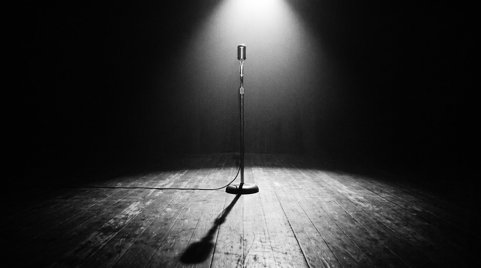 A single microphone under a spotlight on an empty dark stage