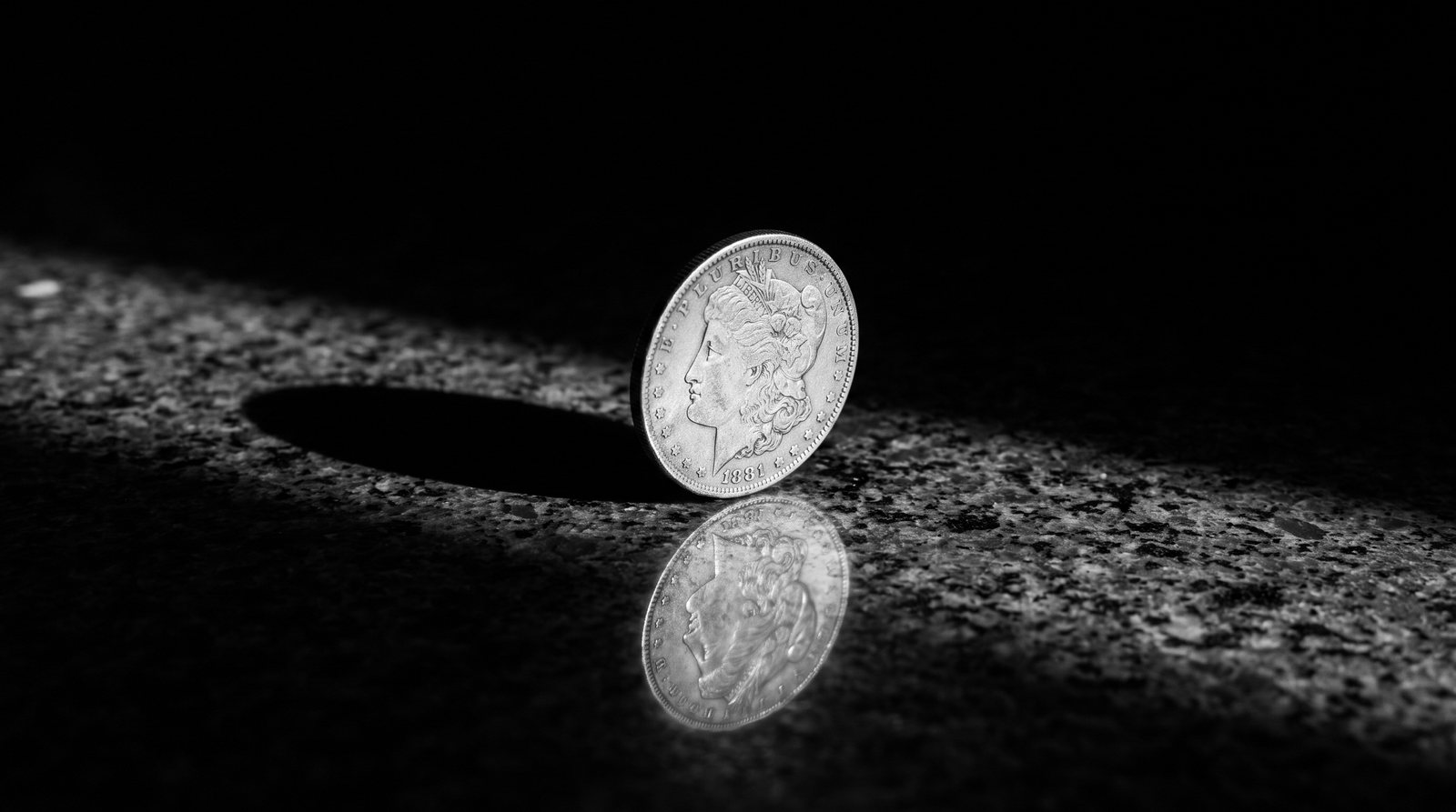 A single coin standing upright on its edge under a spotlight on a dark surface
