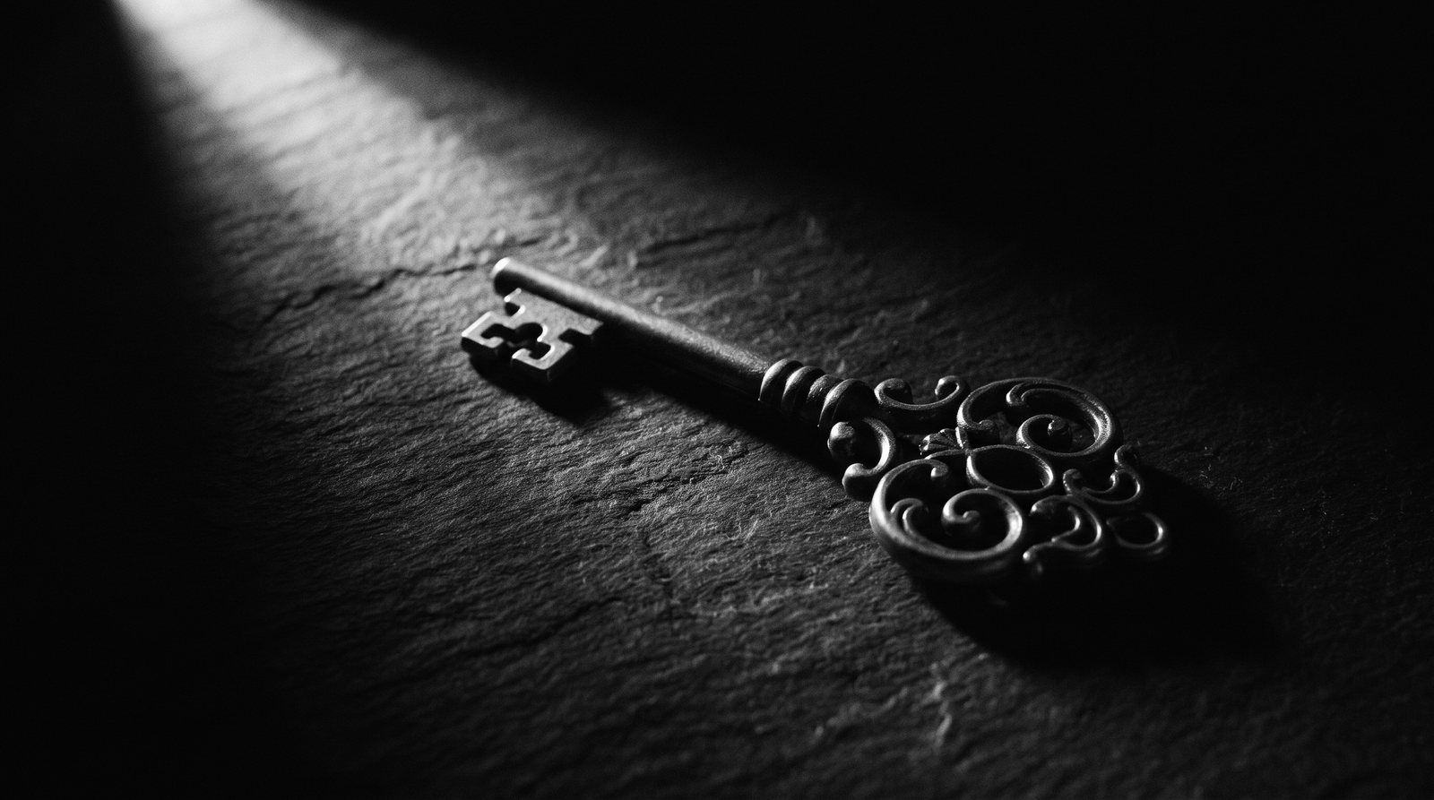 A single ornate brass key on a dark surface catching one shaft of light